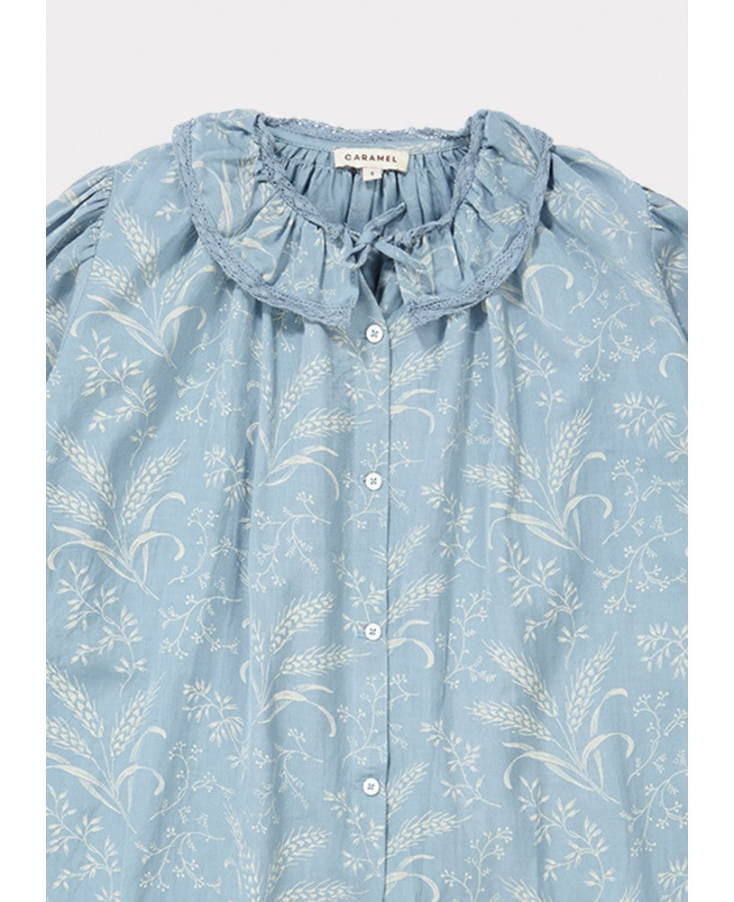 pormenor gola de camisa azul com padrão bege campestre, colarinho plissado largo, mangas compridas com renda nos punhos, pregas na frente e nas costas