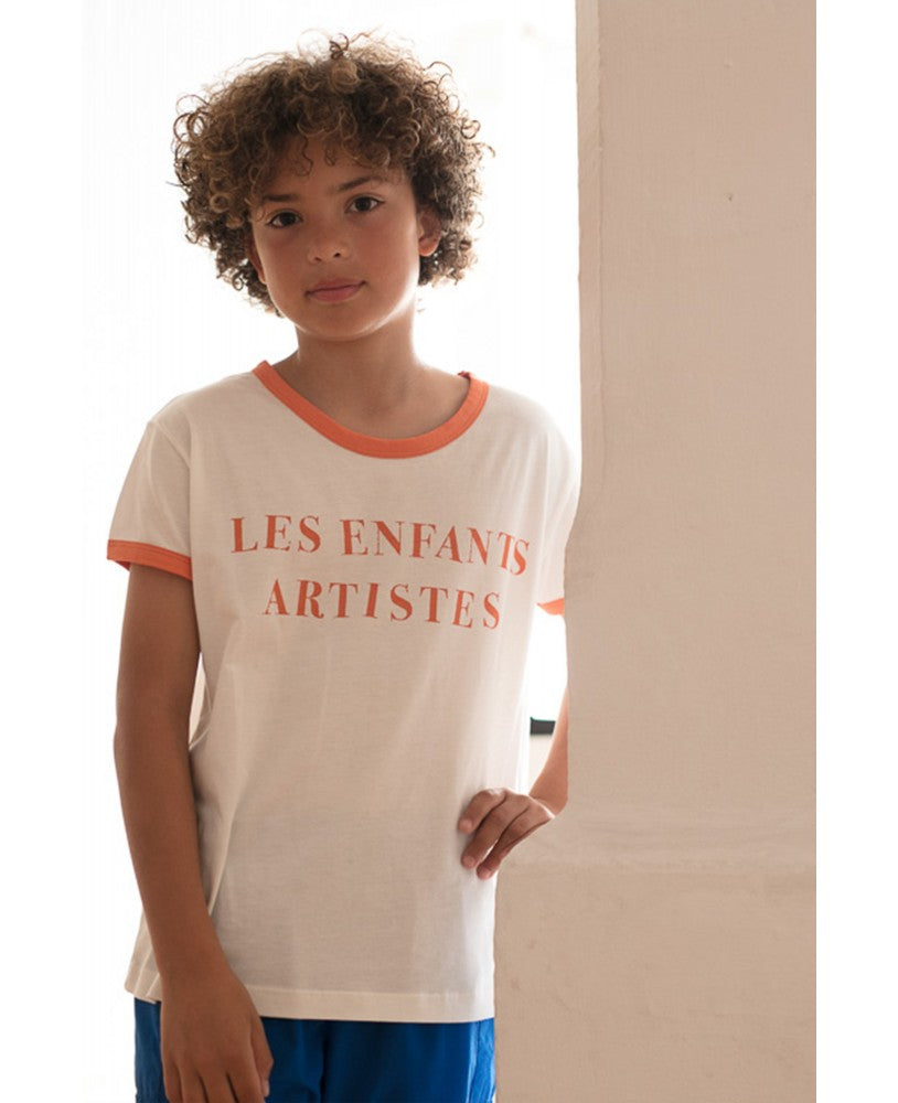 rapaz com t-branca estampada a laranja " les enfants artistes" e calças azuis