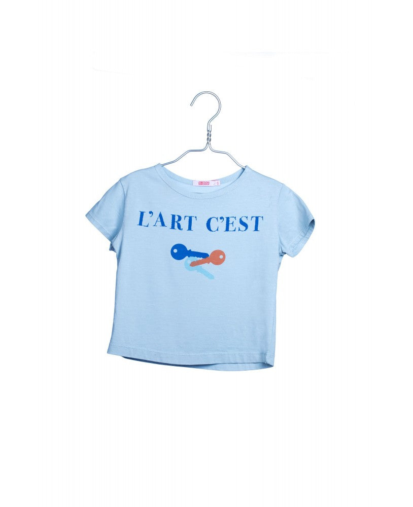 t-shirt em algodão orgânico, azul clara com estampagem "l'art c'est " e chaves em azul escuro, laranja e turquesa