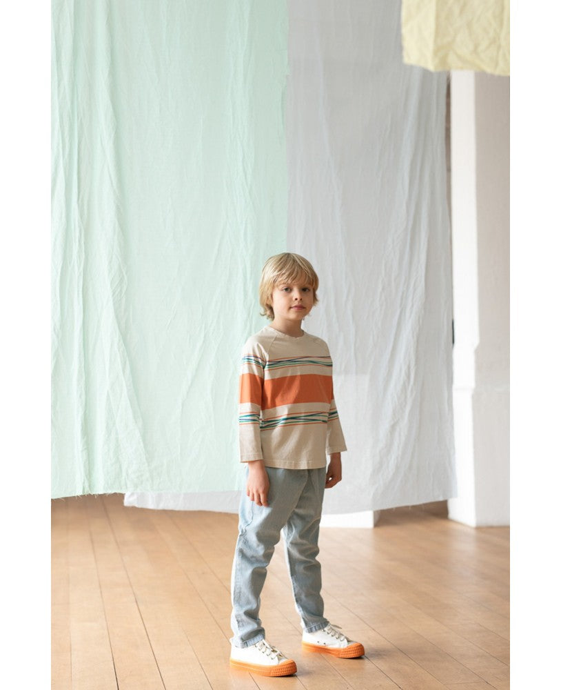 menino vestido com longsleeve bege com riscas coloridas, calças de ganga e ténis brancos e laranja