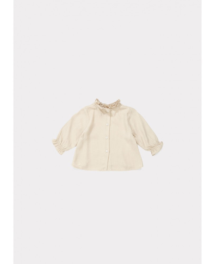 Costas de blusa bebé bege, gola redonda com folho na gola e no punho, botões na parte de trás, silhueta fluída